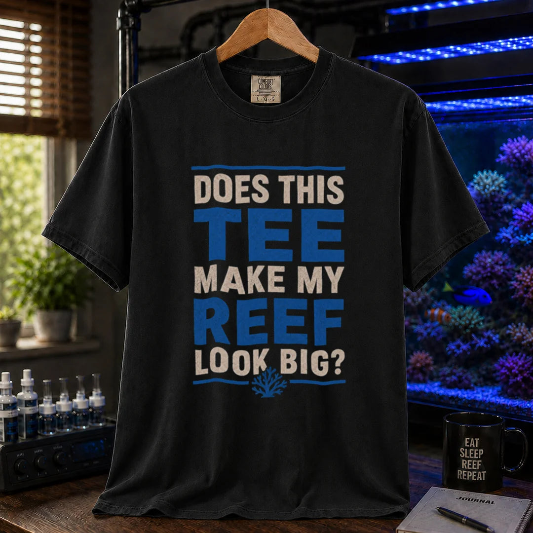 Saltwater aquarium graphic t-shirt featuring distressed white and blue block typography reading Does This Tee Make My Reef Look Big? with a small coral icon printed on a black tee displayed in a reef room setting