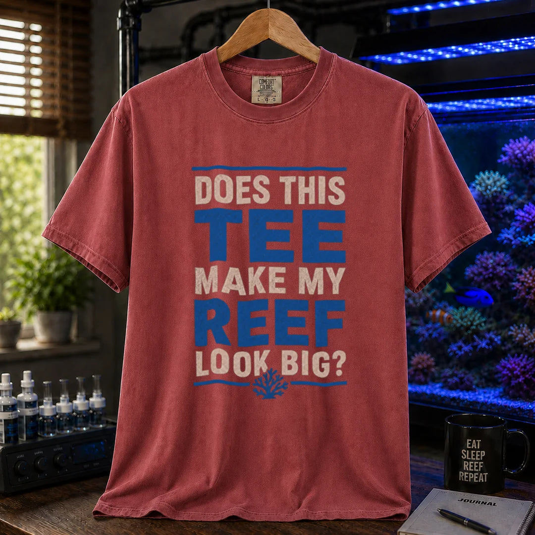 Saltwater aquarium graphic t-shirt featuring distressed white and blue block typography reading Does This Tee Make My Reef Look Big? with a small coral icon printed on a maroon, red tee displayed in a reef room setting