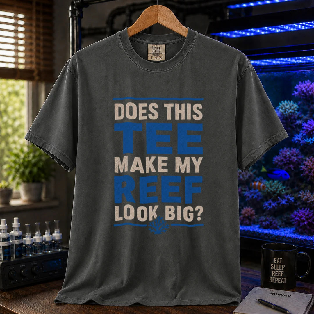 Saltwater aquarium graphic t-shirt featuring distressed white and blue block typography reading Does This Tee Make My Reef Look Big? with a small coral icon printed on a dark grey tee displayed in a reef room setting