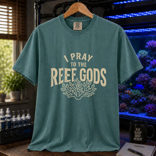 Saltwater aquarium graphic t-shirt featuring distressed cream typography reading I Pray To The Reef Gods with a coral line art graphic printed on a green tee displayed in a reef room setting