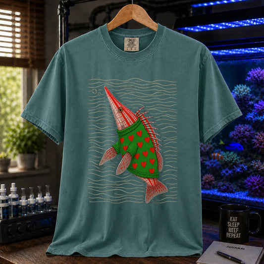 Saltwater aquarium graphic t-shirt featuring a whimsical illustration of a hawkfish wearing a green sweater with red hearts against wavy lines printed on a green tee displayed in a reef room setting