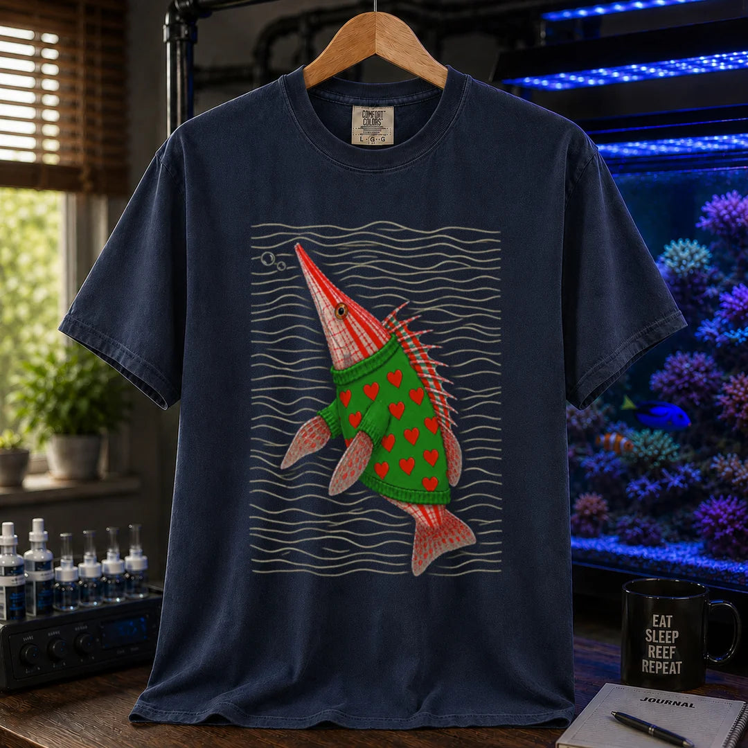Saltwater aquarium graphic t-shirt featuring a whimsical illustration of a hawkfish wearing a green sweater with red hearts against wavy lines printed on a navy tee displayed in a reef room setting