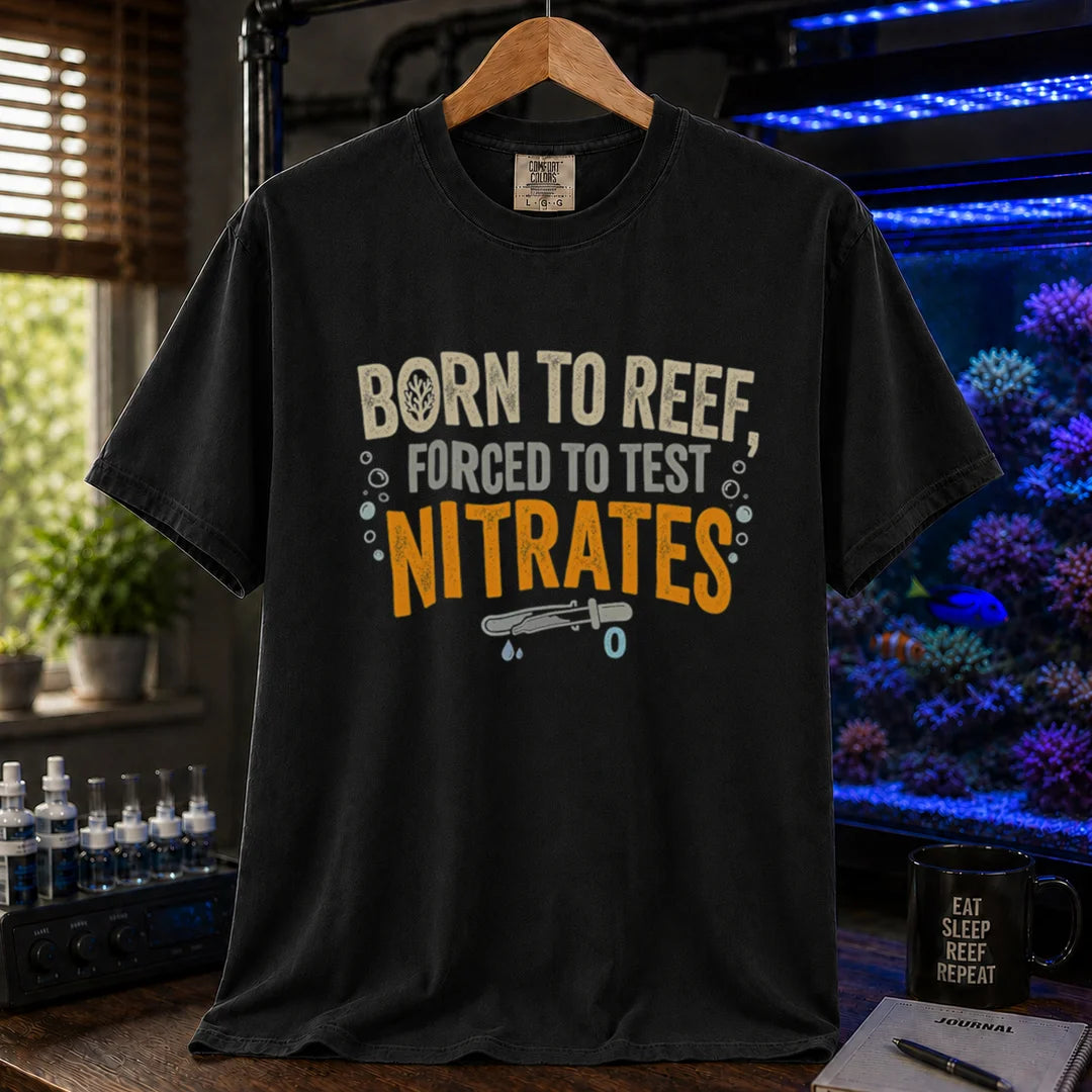 Saltwater aquarium graphic t-shirt featuring distressed cream, gray, and yellow-orange typography reading Born To Reef, Forced To Test Nitrates with a test vial icon printed on a black tee displayed in a reef room setting