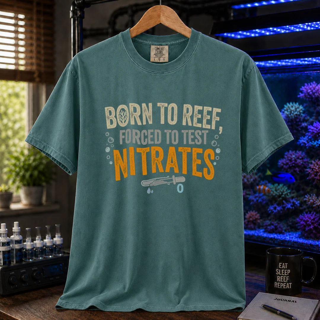 Saltwater aquarium graphic t-shirt featuring distressed cream, gray, and yellow-orange typography reading Born To Reef, Forced To Test Nitrates with a test vial icon printed on a green tee displayed in a reef room setting