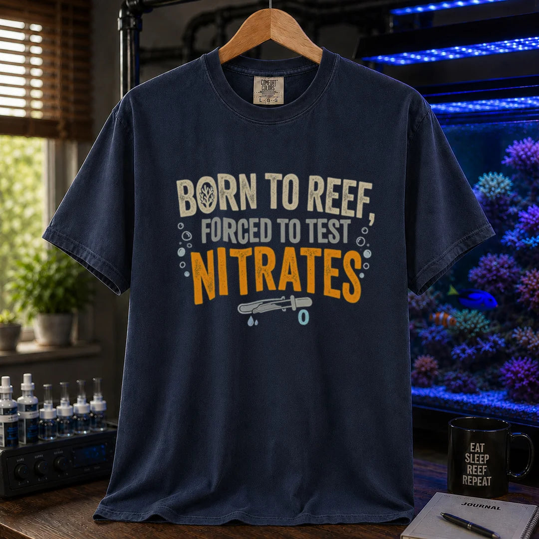 Saltwater aquarium graphic t-shirt featuring distressed cream, gray, and yellow-orange typography reading Born To Reef, Forced To Test Nitrates with a test vial icon printed on a navy tee displayed in a reef room setting