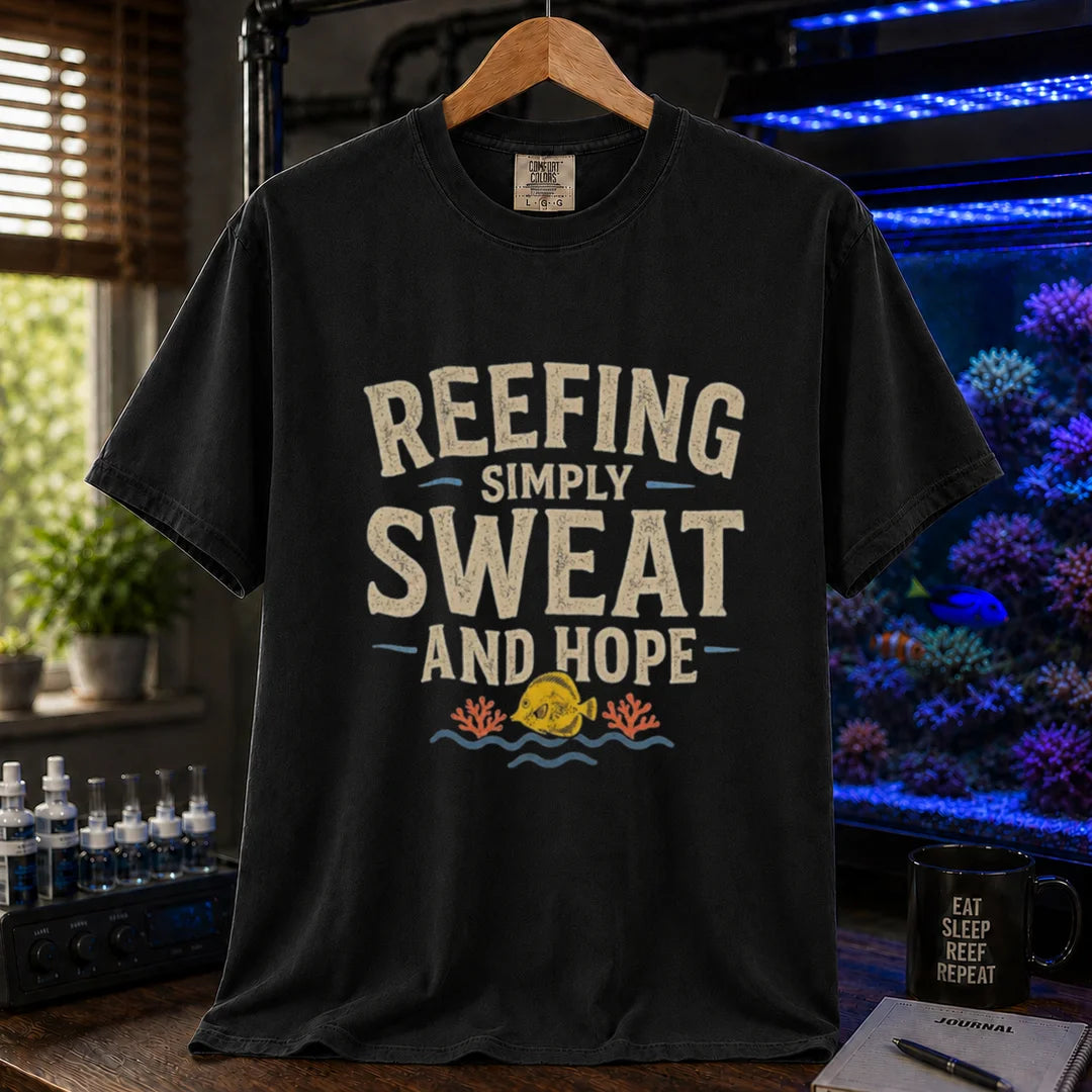 Saltwater aquarium graphic t-shirt featuring distressed cream typography reading Reefing: Simply Sweat And Hope with a yellow tang and coral illustration printed on a black tee displayed in a reef room setting