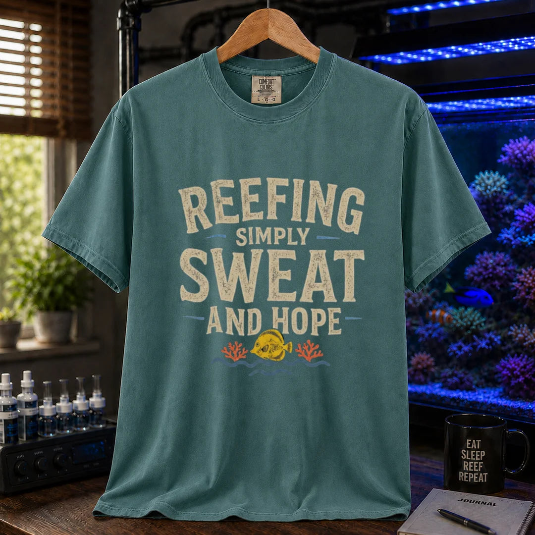 Saltwater aquarium graphic t-shirt featuring distressed cream typography reading Reefing: Simply Sweat And Hope with a yellow tang and coral illustration printed on a green tee displayed in a reef room setting