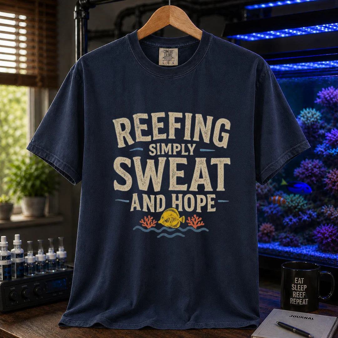 Saltwater aquarium graphic t-shirt featuring distressed cream typography reading Reefing: Simply Sweat And Hope with a yellow tang and coral illustration printed on a navy tee displayed in a reef room setting