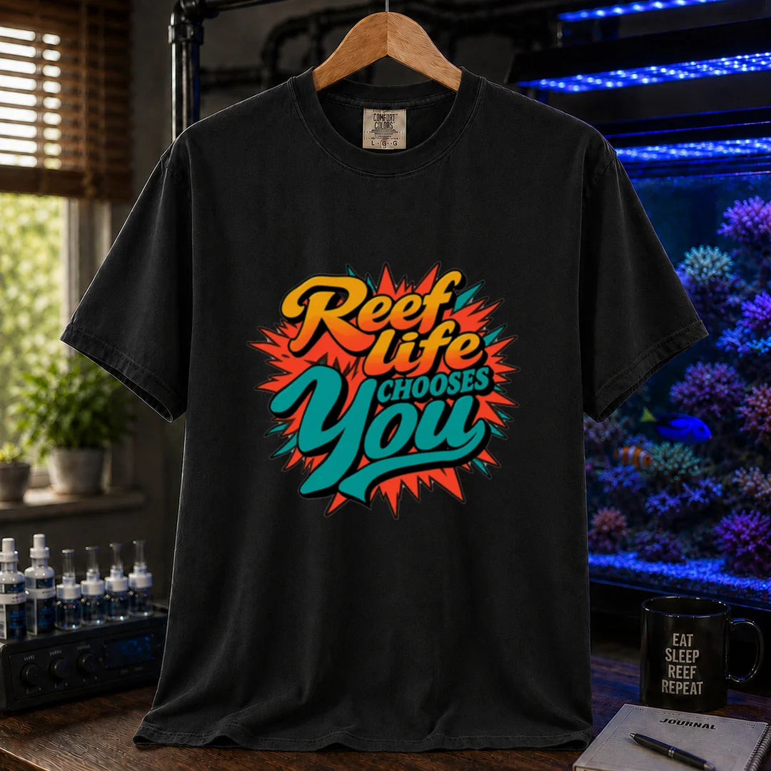 Saltwater aquarium graphic t-shirt featuring vibrant yellow, orange, and teal retro pop-art typography reading Reef Life Chooses You with a red starburst design printed on a black tee displayed in a reef room setting