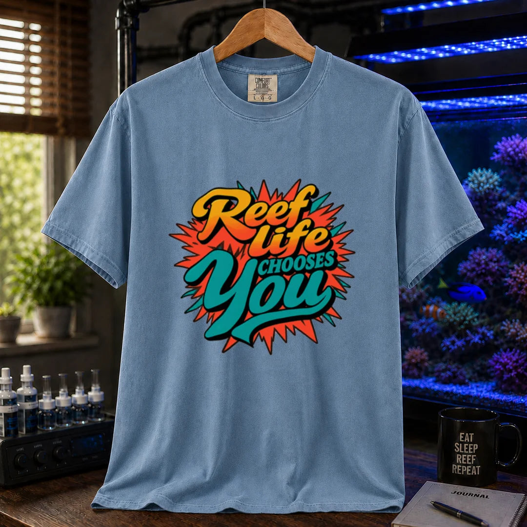 Saltwater aquarium graphic t-shirt featuring vibrant yellow, orange, and teal retro pop-art typography reading Reef Life Chooses You with a red starburst design printed on a blue tee displayed in a reef room setting