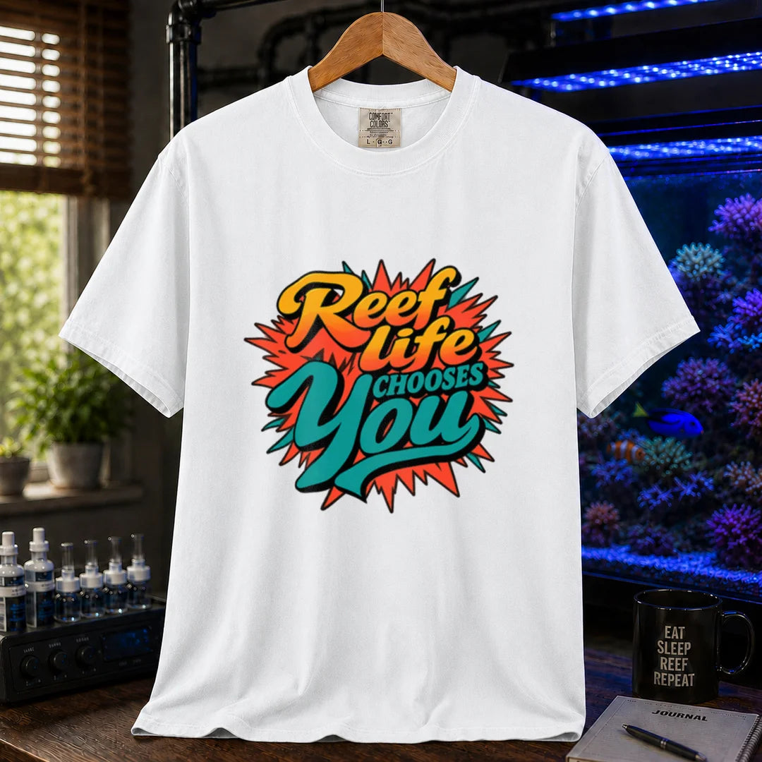 Saltwater aquarium graphic t-shirt featuring vibrant yellow, orange, and teal retro pop-art typography reading Reef Life Chooses You with a red starburst design printed on a white tee displayed in a reef room setting