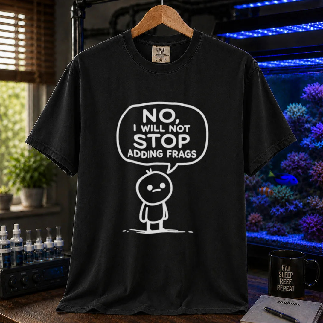 Saltwater aquarium graphic t-shirt featuring a white line-art cartoon character and speech bubble reading No, I Will Not Stop Adding Frags printed on a black tee displayed in a reef room setting
