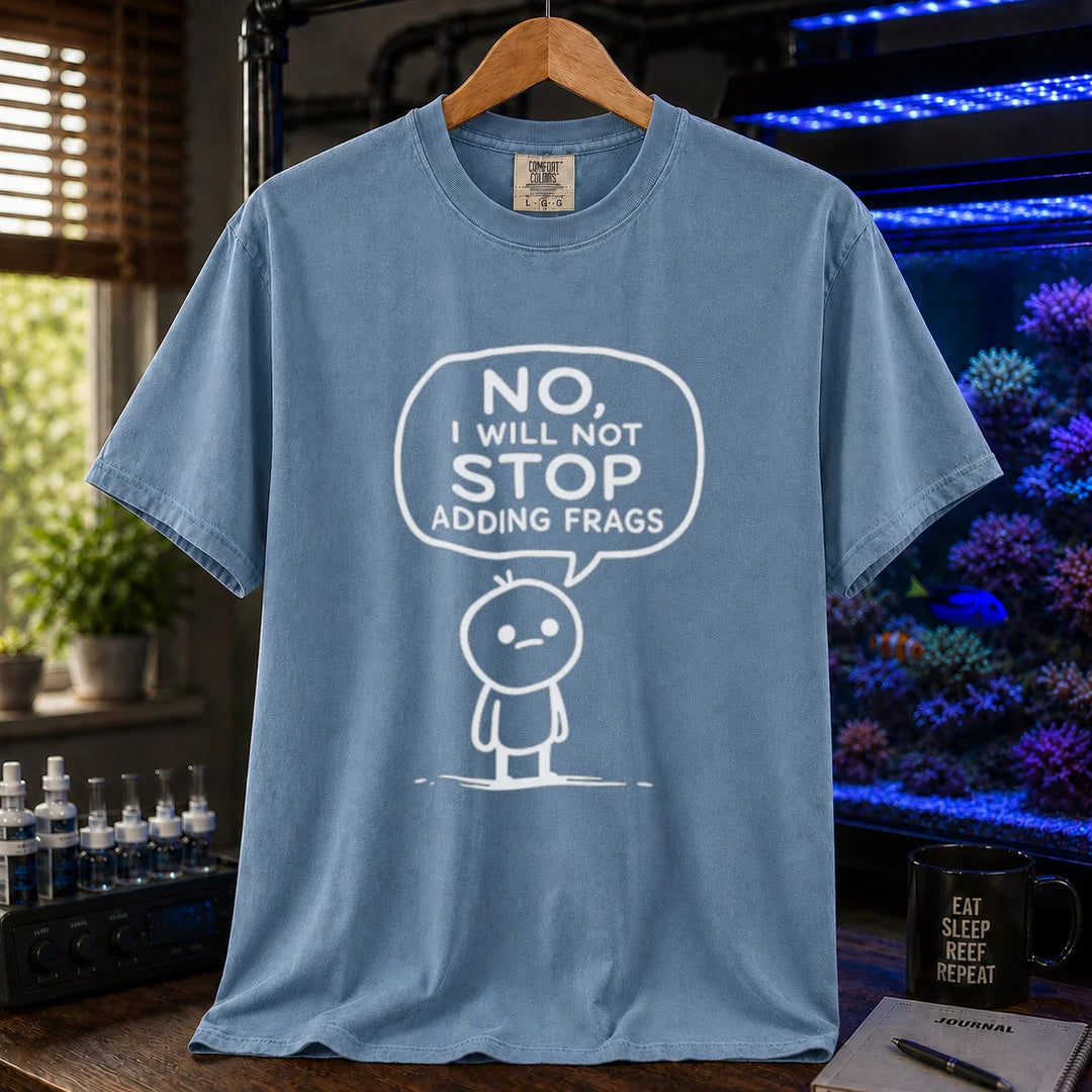 Saltwater aquarium graphic t-shirt featuring a white line-art cartoon character and speech bubble reading No, I Will Not Stop Adding Frags printed on a blue tee displayed in a reef room setting