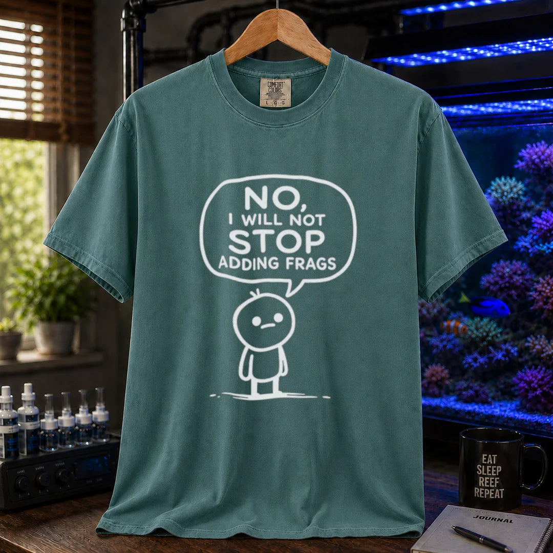 Saltwater aquarium graphic t-shirt featuring a white line-art cartoon character and speech bubble reading No, I Will Not Stop Adding Frags printed on a green tee displayed in a reef room setting