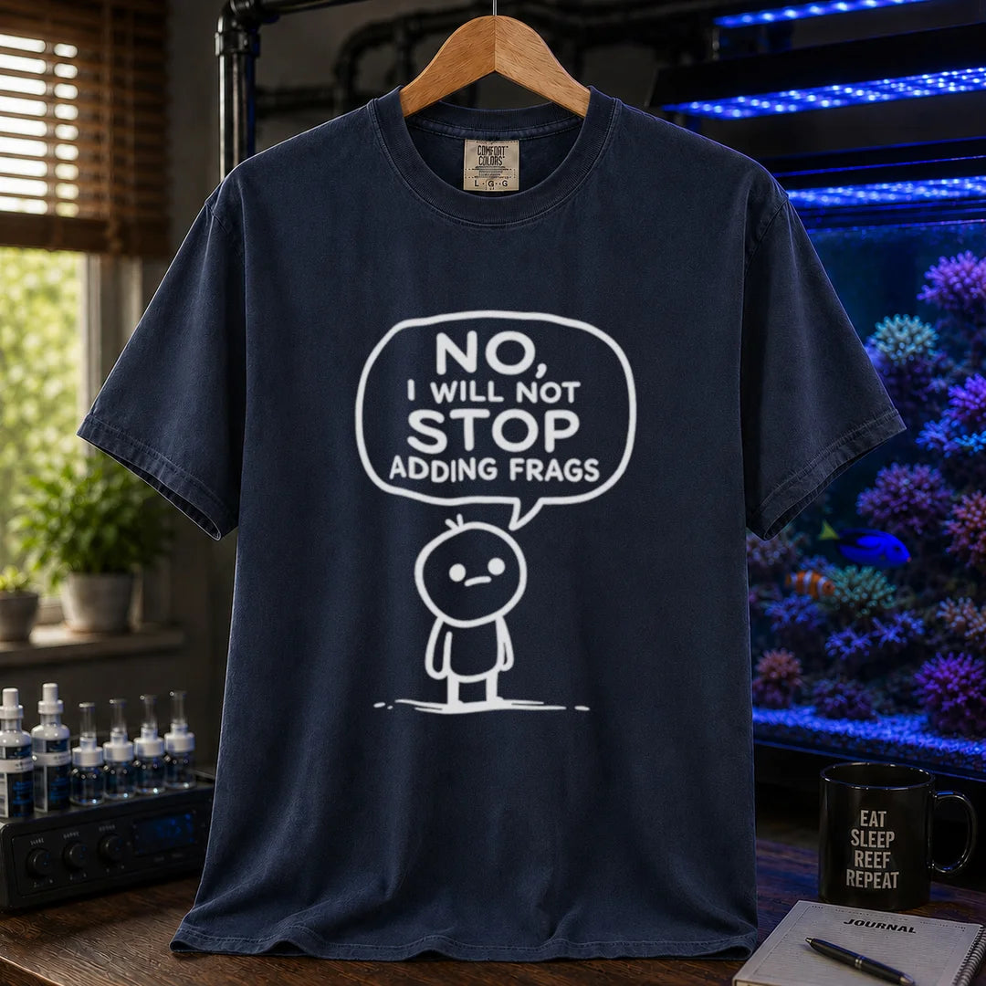 Saltwater aquarium graphic t-shirt featuring a white line-art cartoon character and speech bubble reading No, I Will Not Stop Adding Frags printed on an navy tee displayed in a reef room setting