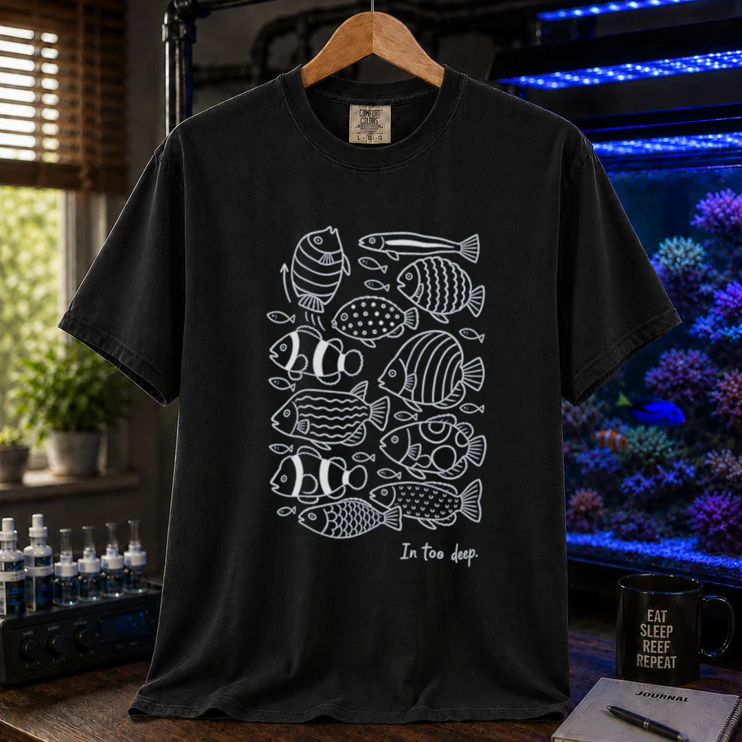 Saltwater aquarium graphic t-shirt featuring a minimalist white line-art pattern of various reef fish and the caption In too deep. printed on a black tee displayed in a reef room setting