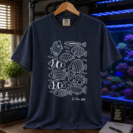 Saltwater aquarium graphic t-shirt featuring a minimalist white line-art pattern of various reef fish and the caption In too deep. printed on a navy tee displayed in a reef room setting