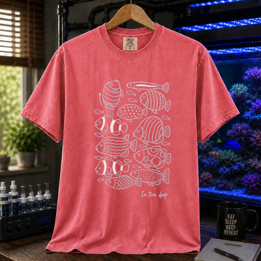Saltwater aquarium graphic t-shirt featuring a minimalist white line-art pattern of various reef fish and the caption In too deep. printed on a watermelon tee displayed in a reef room setting