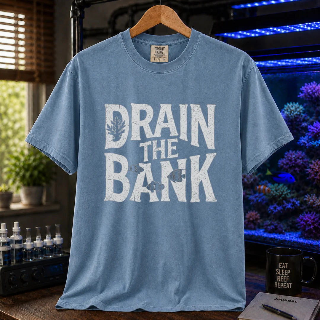 Saltwater aquarium graphic t-shirt featuring distressed white block lettering reading Drain The Bank with subtle fish and coral shapes on a blue shirt