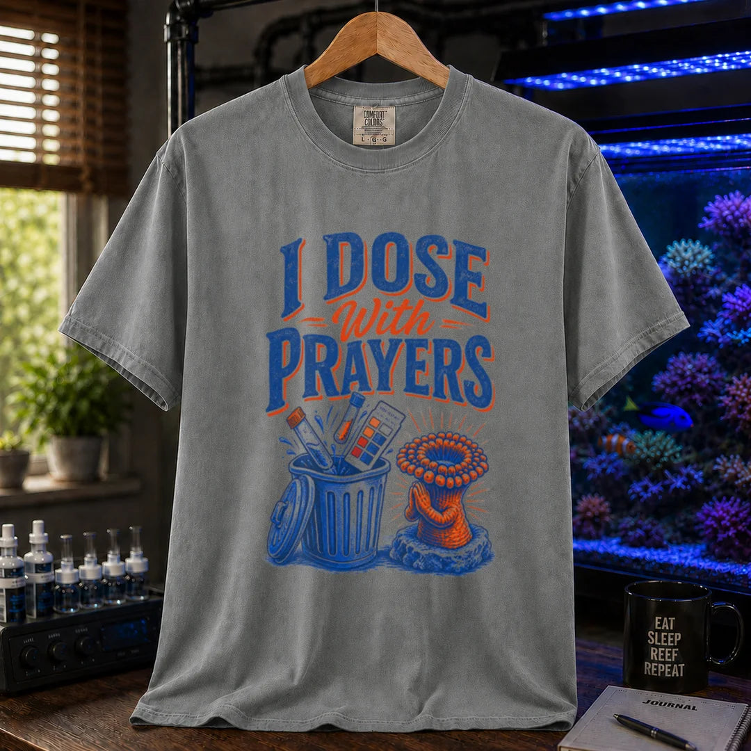 Saltwater aquarium graphic t-shirt featuring typography reading I Dose With Prayers above an illustration of test kits in a trash can and a praying coral polyp on a grey shirt