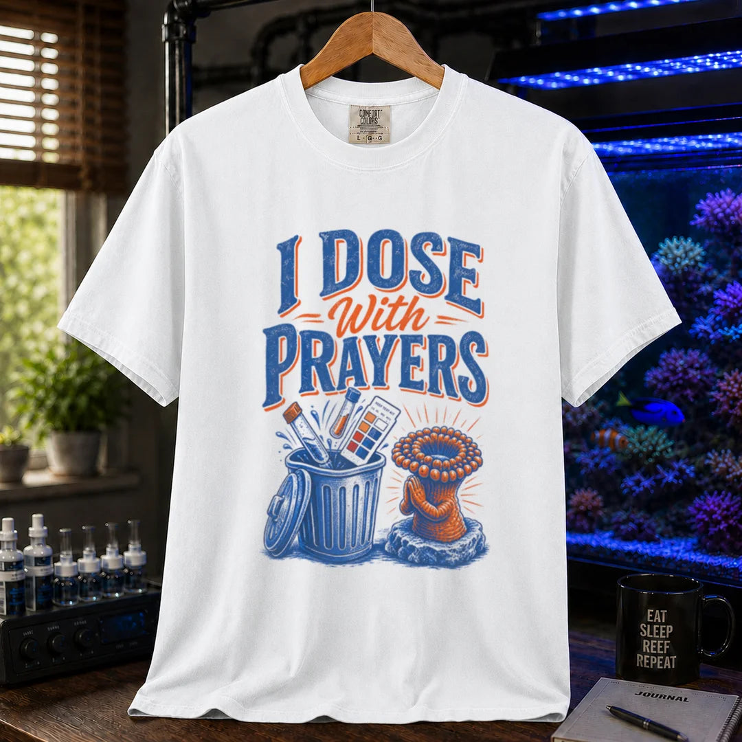 Saltwater aquarium graphic t-shirt featuring typography reading I Dose With Prayers above an illustration of test kits in a trash can and a praying coral polyp on a white shirt