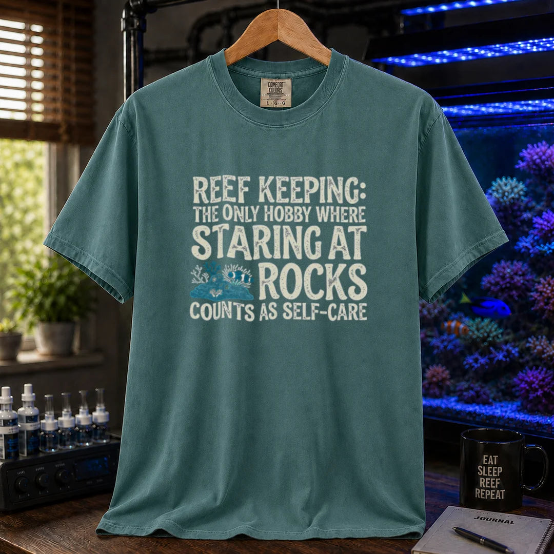 Saltwater aquarium graphic t-shirt featuring distressed typography reading Reef Keeping The Only Hobby Where Staring At Rocks Counts As Self-Care with a small rock and coral illustration on a green shirt