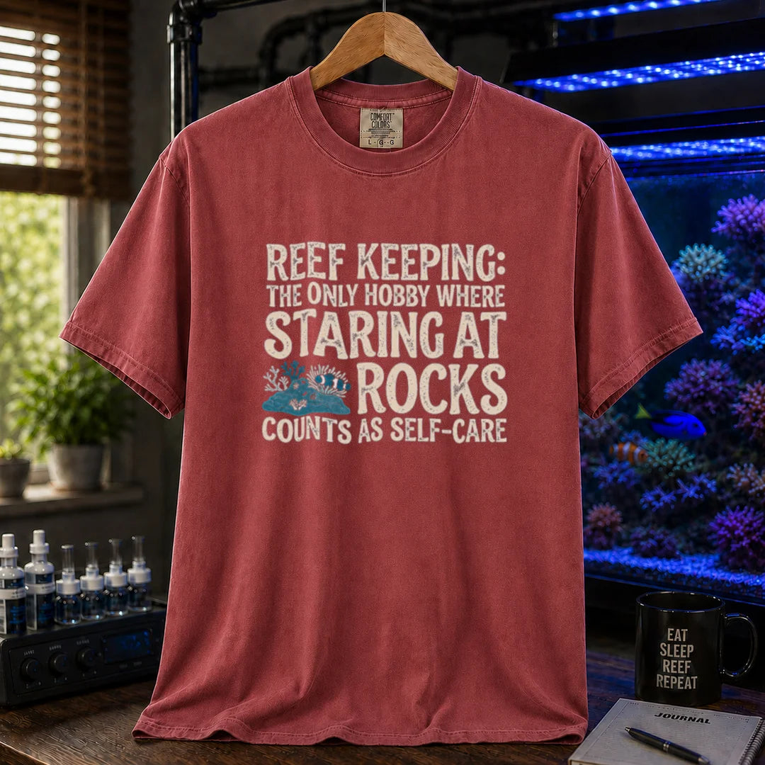 Saltwater aquarium graphic t-shirt featuring distressed typography reading Reef Keeping The Only Hobby Where Staring At Rocks Counts As Self-Care with a small rock and coral illustration on a maroon, red shirt