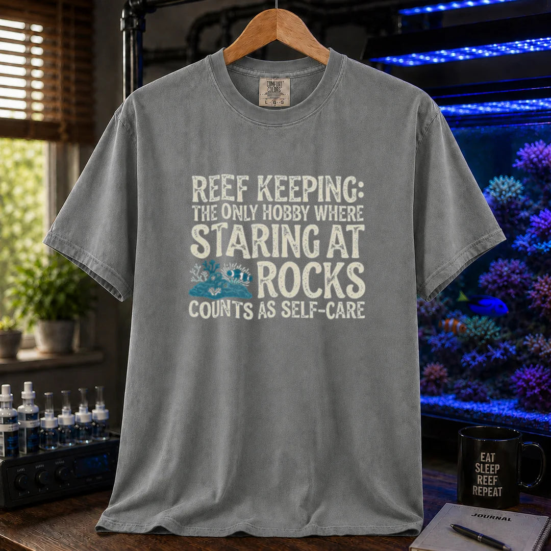 Saltwater aquarium graphic t-shirt featuring distressed typography reading Reef Keeping The Only Hobby Where Staring At Rocks Counts As Self-Care with a small rock and coral illustration on a grey shirt