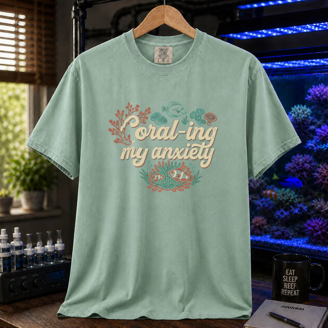 Saltwater aquarium graphic t-shirt featuring handwritten typography reading Coral-ing My Anxiety with colorful coral and fish illustrations on a light green shirt