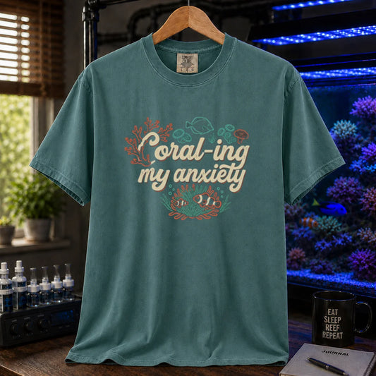 Saltwater aquarium graphic t-shirt featuring handwritten typography reading Coral-ing My Anxiety with colorful coral and fish illustrations on a green shirt
