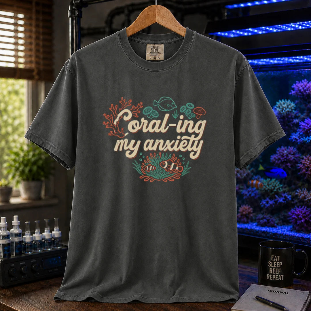 Saltwater aquarium graphic t-shirt featuring handwritten typography reading Coral-ing My Anxiety with colorful coral and fish illustrations on a dark grey shirt