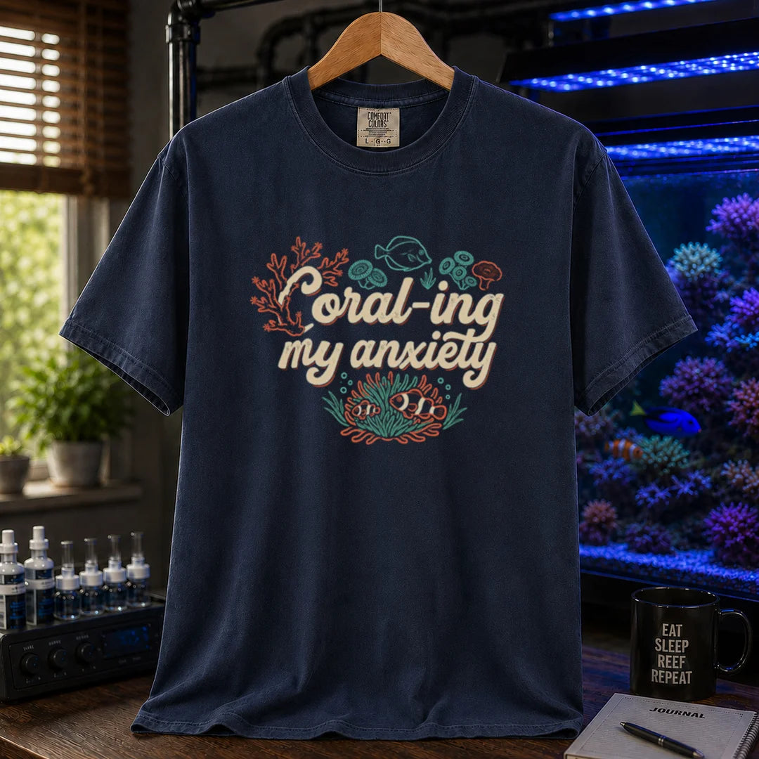 Saltwater aquarium graphic t-shirt featuring handwritten typography reading Coral-ing My Anxiety with colorful coral and fish illustrations on a navy shirt