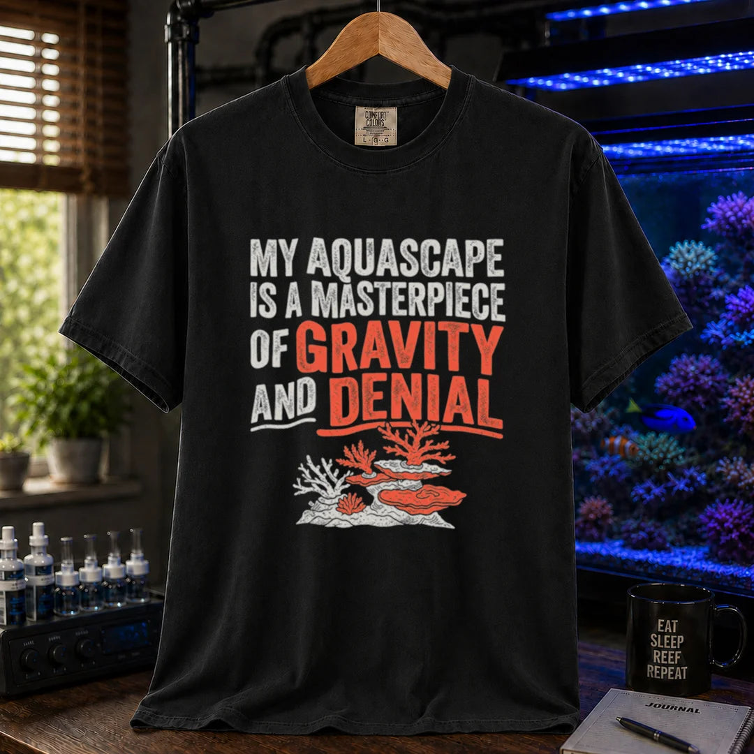 Saltwater aquarium graphic t-shirt featuring distressed typography reading My Aquascape Is A Masterpiece Of Gravity And Denial above a coral illustration on a black shirt