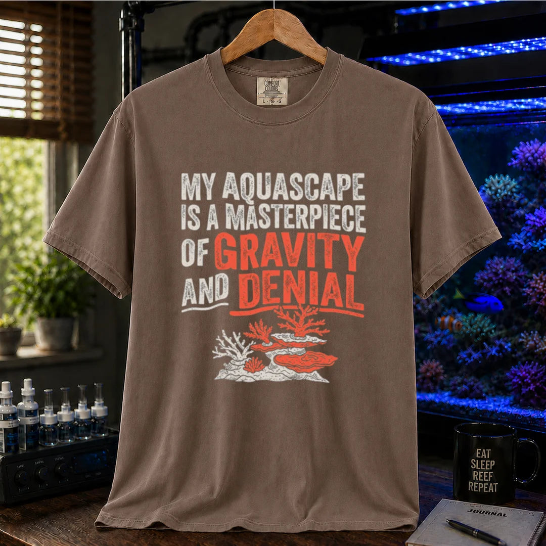 Saltwater aquarium graphic t-shirt featuring distressed typography reading My Aquascape Is A Masterpiece Of Gravity And Denial above a coral illustration on a brown shirt