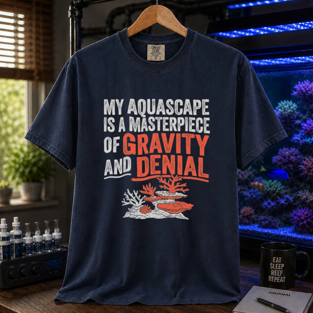 Saltwater aquarium graphic t-shirt featuring distressed typography reading My Aquascape Is A Masterpiece Of Gravity And Denial above a coral illustration on a navy shirt
