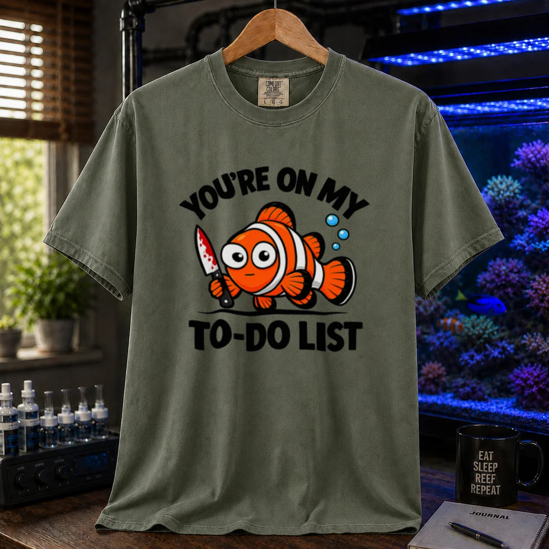 Saltwater aquarium graphic t-shirt featuring bold typography reading You're On My To-Do List framing an illustration of a clownfish holding a knife on a military green shirt